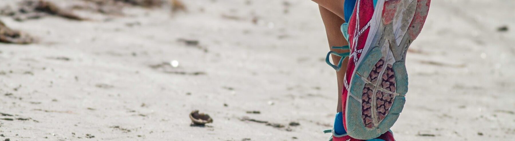 woman in white red and blue sneakers sitting on white sand during daytime